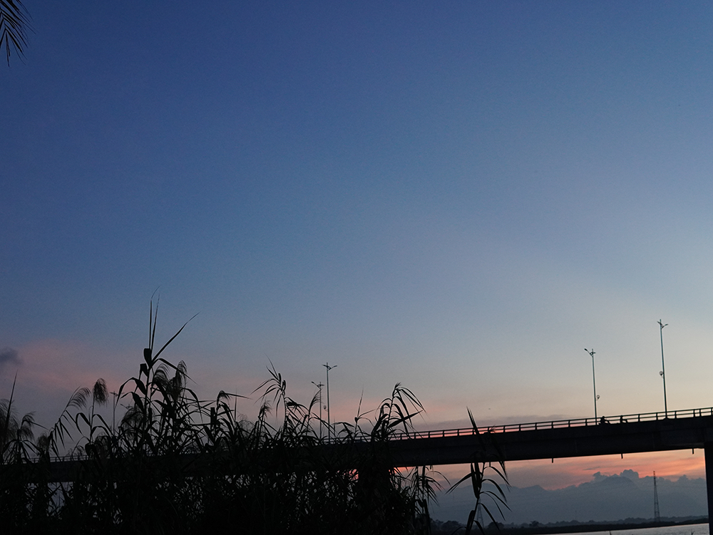 Nestled along the serene riverbanks of Hoi An, the Cam Kim Bridge takes on a mesmerizing new light in the magical twilight, its elegant structure bathed in the glow of the setting sun. This captivating sight, framed by the city's lush, verdant surroundings, invites visitors to discover the historic landmarks, cultural treasures, and natural beauty of this beloved Vietnamese destination.