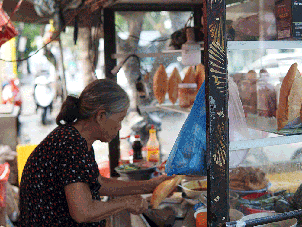 In the street of Hoi An, an elderly lady skillfully prepares the signature banh mi, one of the most famlous Hoi An food.