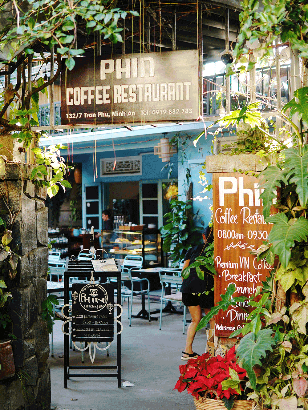 Inviting exterior of the Phin Coffee restaurant in Hoi An, Vietnam, showcasing its sleek, modern design with a warm, yellow-toned ambiance and lush, verdant plants surrounding the entrance - a captivating destination for experiencing the best coffee in the historic town.
